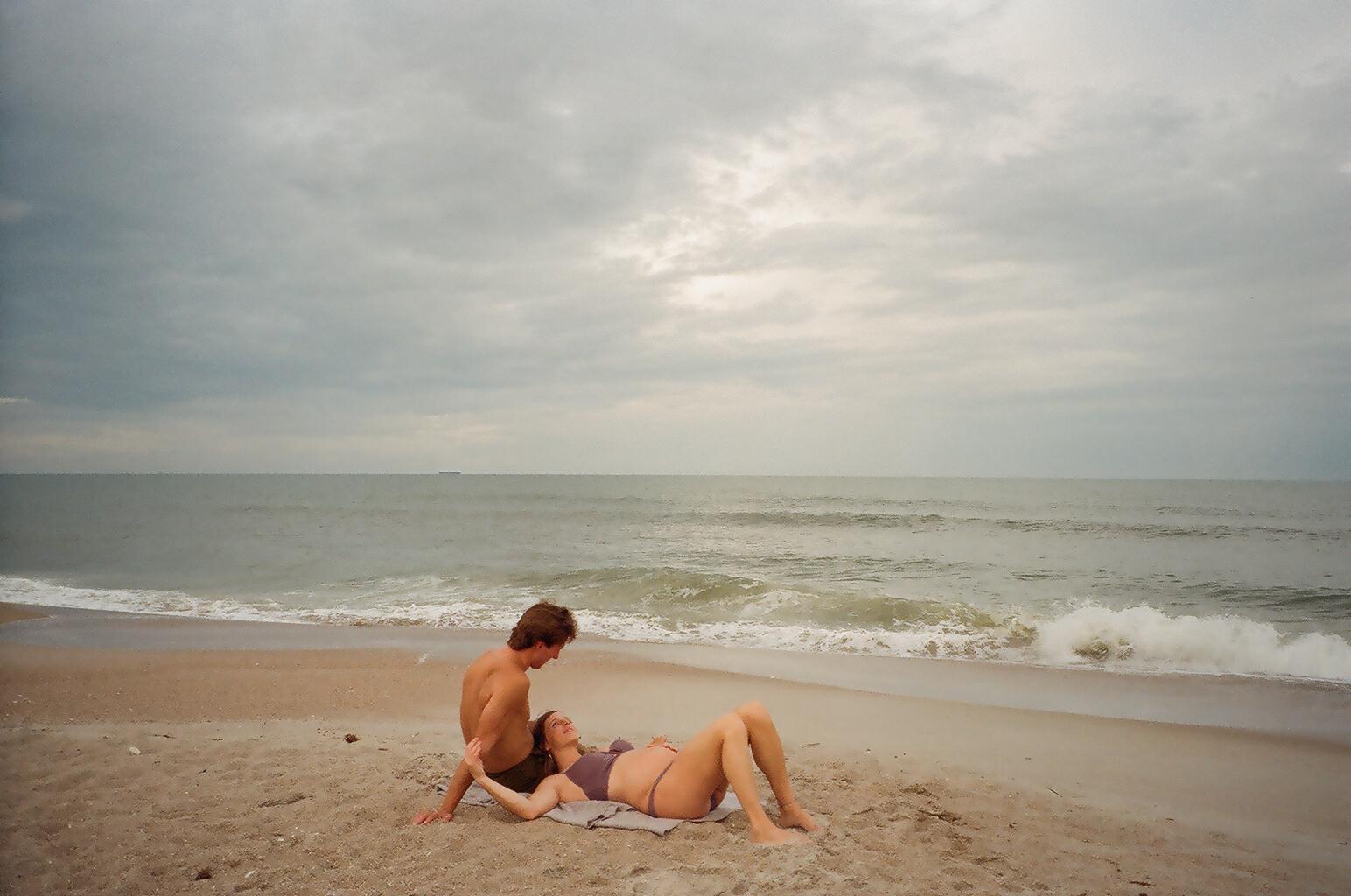 Pregnant Couple Laying in Sand by Ocean