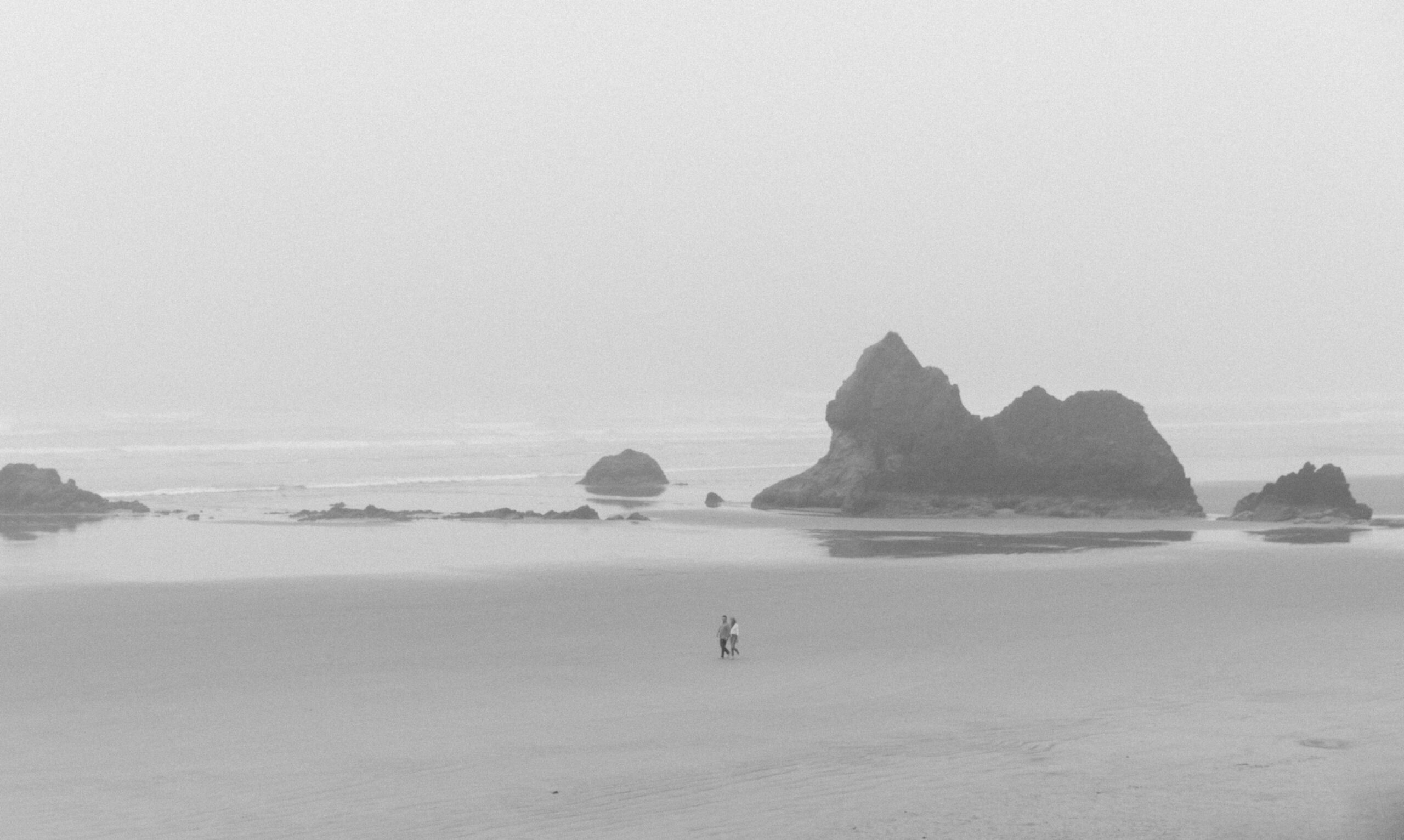 Black and white photo of couple walking along coast